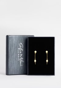Goldfarbene Ohrringe mit runden Steckern und hängenden Ketten, die einen zentralen klaren Kristall tragen. Präsentiert in einer strukturierten schwarzen Box.