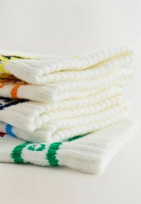 Biele pletené ponožky uspořádané neatly, s barevnými proužky v žltej, oranžovej, modrej a zelenej farbe. Mäkka textúra, ribovaný dizajn na leme.