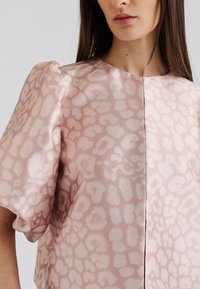 Rosa Bluse mit glänzender Textur, die ein dezentes helles Leopardenmuster aufweist, kurze Puffärmel und einen runden Ausschnitt hat.