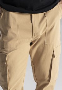 Beżowe spodnie cargo z wieloma kieszeniami, wykonane z trwałej bawełny. Charakteryzują się prostym krojem oraz widocznymi detalami szwów.