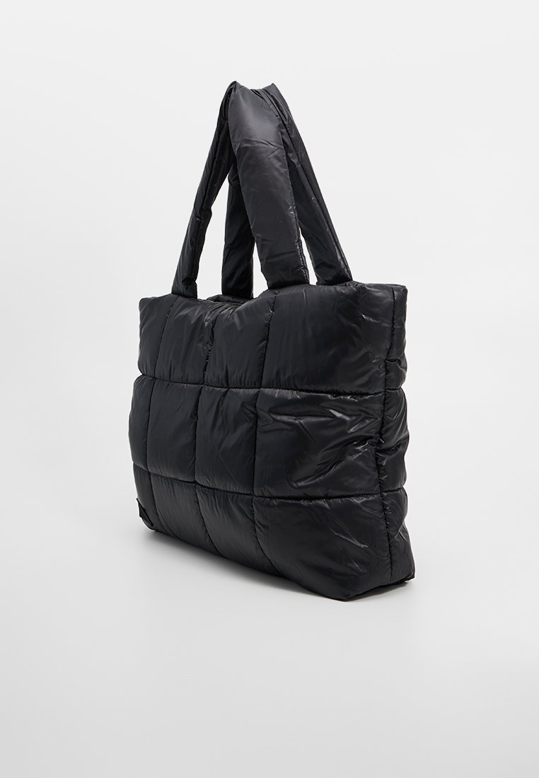 Schwarze, gepolsterte Tragetasche mit einem gesteppte Design, ausgestattet mit zwei kurzen Griffen, aus glänzendem Nylonmaterial gefertigt, das eine weiche und gepolsterte Textur bietet.