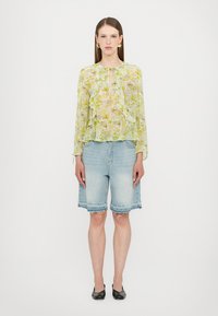 Sheer yellow-green blouse with ruffles, paired with light blue denim bermuda shorts. Model wears black flats and minimal jewelry.