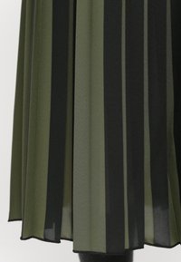 Ourlet de jupe plissée avec de larges rayures verticales en tissu noir et vert olive.