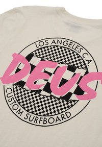Cream-colored t-shirt featuring a circular graphic with a checkerboard pattern and bold pink "DEUS" text, labeled "LOS ANGELES C.A." and "CUSTOM SURFBOARD."