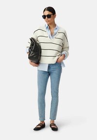 Sweter w białe paski, jasnoniebieska koszula na guziki, obcisłe jasne jeansy oraz czarne baleriny. W ręku trzyma czarną miękką torbę. Na nosie okulary przeciwsłoneczne.