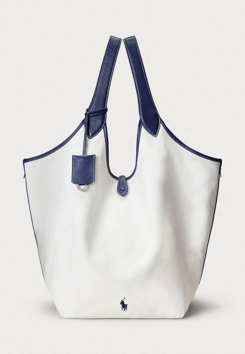 Bolso tote hecho de lona blanca con detalles en cuero azul marino, que cuenta con dos asas, un pequeño estuche adjunto y un logo en la parte inferior.