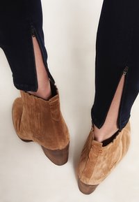 Bruna mocka ankelstövlar med en kraftig klack, matchade med mörkblå jeans med sidizipper vid fållen, som visar en slät yta.