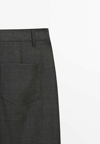 Pantalon en tissu gris foncé avec une seule poche arrière et une boucle de ceinture visible sur fond blanc.