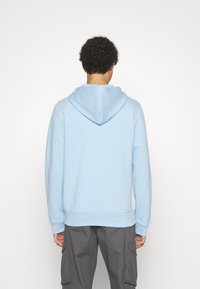 Šviesiai mėlyna hoodie su šnoru, raukšlėtais rankogaliais ir hemu. Minkšta tekstūra, užtrauktuko dizainas ir minimalistiškas stilius.