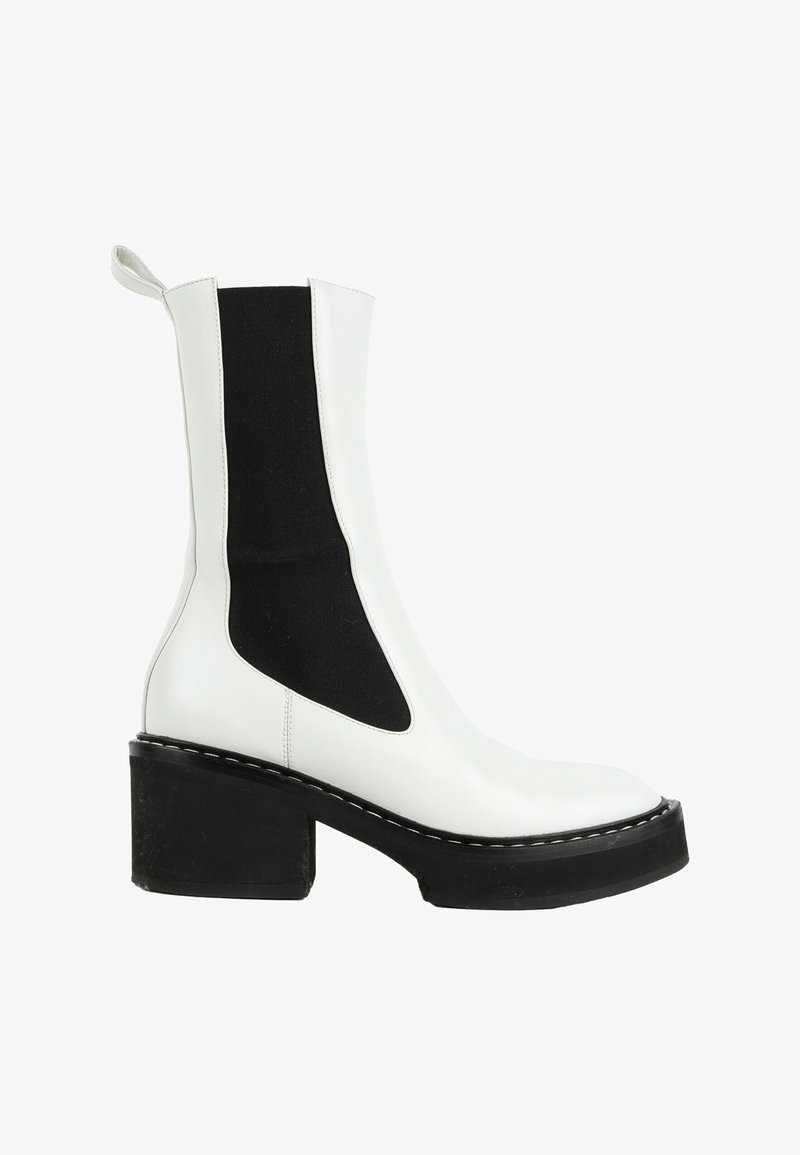 Bottine blanche en cuir avec un panneau latéral élastique noir et un épais talon bloc noir sur fond blanc.