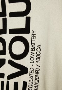 Tissu tricoté crème avec de grandes impressions en texte noir. Comprend des lettres en gras et des détails comme "LOW BATTERY" et "100CCA".