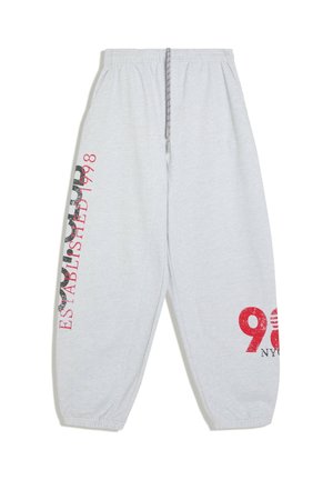 Lichtgrijze joggingbroek met elastische boorden en tailleband, trekkoortje en rode en zwarte tekstgrafieken op het linkerbeen en de rechterkuit.
