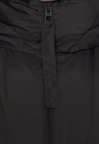 Černá péřová bunda s prošívanou texturou, s předním zipem a logem. Hladký materiál s vysokým límcem pro větší teplo.