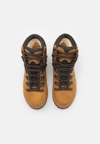 Bottes de randonnée en daim marron avec des accents en tissu foncé, dotées d'œillets en métal, de lacets marron et d'une semelle texturée pour une traction et une stabilité optimales.