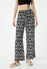 Valkoiset ja mustat leveät housut, joissa on abstrakti geometrinen kuvio, joustava vyötärö ja kevyestä kankaasta valmistettu. Yhdistetty kevyisiin sandaaleihin.