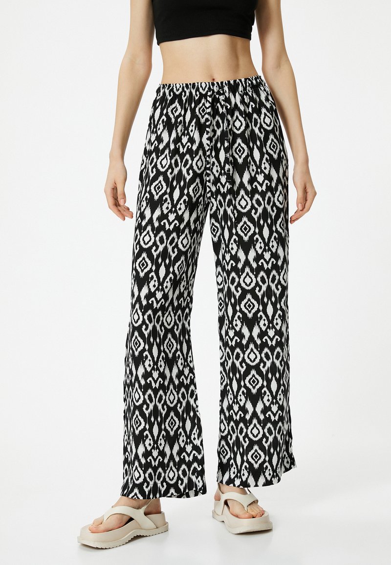 Valkoiset ja mustat leveät housut, joissa on abstrakti geometrinen kuvio, joustava vyötärö ja kevyestä kankaasta valmistettu. Yhdistetty kevyisiin sandaaleihin.