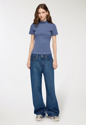 Maglione a girocollo attillato azzurro chiaro a maniche corte, abbinato a jeans in denim blu a vestibilità comoda e sneakers grigie. Texture liscia, design casual.