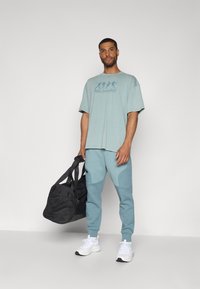 Under Armour UNSTOPPABLE FLEECE - Tracksuit bottoms - jasper blue/serpentine/black