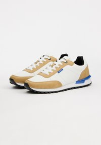 Zapatillas blancas y tan con acentos de ante, interior negro, detalle en el talón azul y suela de goma negra; cordones pasados por ojales estándar.