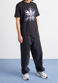Black cotton t-shirt with a graphic of lightning bolts and the Adidas logo on the front, paired with loose-fitting dark jeans and sneakers.