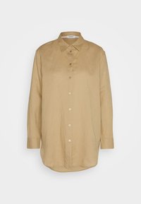 Chemise beige à manches longues avec boutons, col pointu et ourlet arrondi, présentée sur un fond blanc uni.