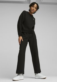 Czarna, teksturowana bluza z długim rękawem i pasujące spodnie. Bluza ma okrągły dekolt, ściągacze na rękawach; spodnie mają luźny krój. Białe trampki dopełniają stylizację.
