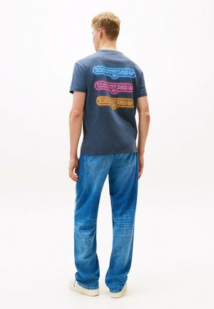 Mørkeblå bomulds T-shirt med farverig "tommy jeans" tekstdesign på ryggen. Parret med lyseblå denim jeans og hvide sneakers.