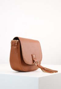 Brun läder crossbody-väska med klaffstängning, vävda axelremmar och en tofsdetalj. Slätt material och medelstor design.