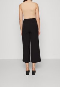 Pantalon noir à jambes larges avec taille haute, tissu lisse, longueur raccourcie et coupe décontractée. Associé à des sandales à talons blocs.