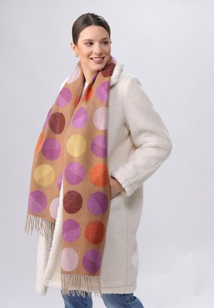 Sciarpa marrone a motivo con grandi cerchi in viola, rosa, arancione e giallo, con frange alle estremità, indossata sopra un cappotto bianco.