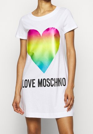 Valkoinen lyhythihainen mekko, jossa suuri sateenkaaren värinen sydän ja "LOVE MOSCHINO" -teksti, yllään seisovalla henkilöllä yksiväristä taustaa vasten.