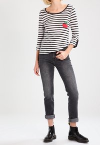 Czarno-biała koszula z długim rękawem w paski z grafiką wiśni, w połączeniu z ciemnymi dżinsami z podwiniętymi mankietami i błyszczącymi czarnymi botkami za kostkę.