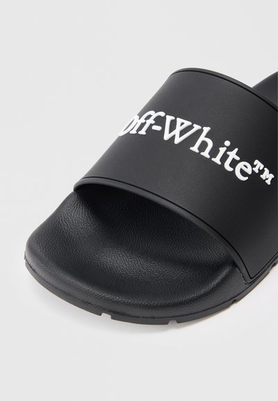 Sandale negre cu talpă plată, având o curea lată cu logo-ul alb „Off-White” embosat. Trecere texturată și suprafață superioară netedă.