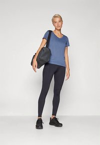 Atlétikai öltözék kék, rövid ujjú, V-nyakú pólóval, fekete leggingssel és fekete tornacipővel, kiegészítve egy fekete sporttáskával.