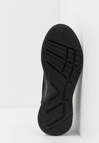 Suola nera di sneaker con gomma texture, caratterizzata da un battistrada a motivo per la presa, accenti lisci e un design minimalista su sfondo bianco.