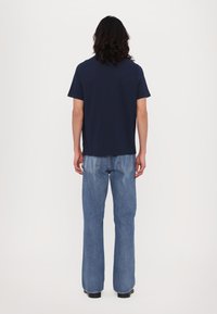 Tricou bleumarin cu mânecă scurtă din bumbac, asortat cu blugi evazați de culoare albastru deschis, cu un efect de decolorare și buzunare cusute la spate.