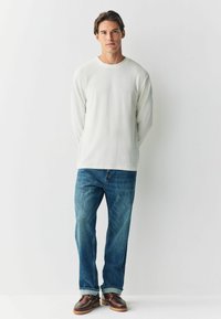 Cămașă gri deschis cu mânecă lungă și guler rotund, purtată împreună cu blugi blue denim și pantofi cu șireturi căprui, cu talpă rezistentă.