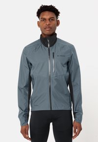 Veste Vaude grise avec un col haut, fermeture éclair complète, design épuré et accents noirs extensibles sur les côtés. Matériau léger et respirant.