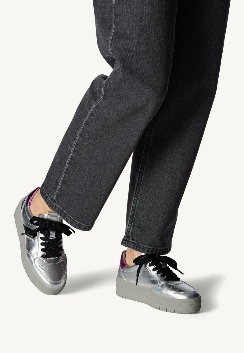 Baskets métalliques argentées avec des lacets noirs, tige texturée et semelle plateforme grise, présentant un accent violet au niveau du talon.