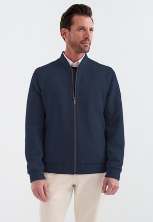 Veste de bombardier navy avec fermeture éclair à l'avant, poignets et ourlet côtelés, et poches latérales. Tissu lisse avec une silhouette moderne et épurée.