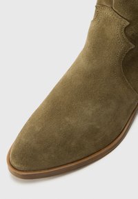 Olivroheline suede pahklöök koos terava varbaga, tikandite ja pruunist kummist tallaga. Sujuv tekstuur ja minimalistlik stiil.