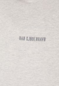 Camiseta de algodón gris claro con texto bordado "HAN KJØBENHAVN" en gris oscuro. La tela tiene una textura suave y lisa.