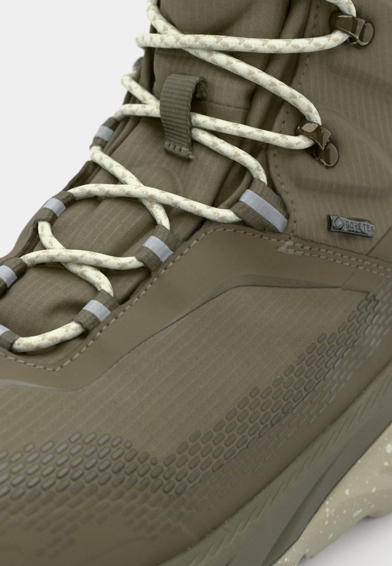 Bruine waterdichte wandelschoen met een getextureerd oppervlak, versterkte neus, elastische veters en een logo patch. Heeft een gevoerde zool met een gespikkeld patroon.