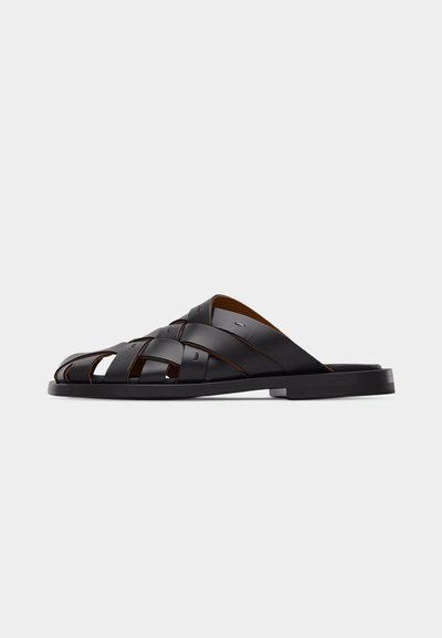 Sandale à enfiler en cuir noir tressé avec bout ouvert, semelle plate et brides croisées, vue de profil sur un fond uni.