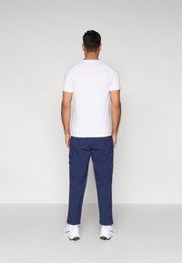 Camiseta blanca de manga corta, combinada con pantalones cargo azul marino con bolsillos laterales, usada con zapatillas deportivas blancas. Diseño sencillo y minimalista.