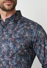 Hemd mit Knopfleiste aus strukturiertem marineblauen Stoff, mit einem floralen Muster in Rot-, Pink- und Grautönen, spitzem Kragen und langen Ärmeln.