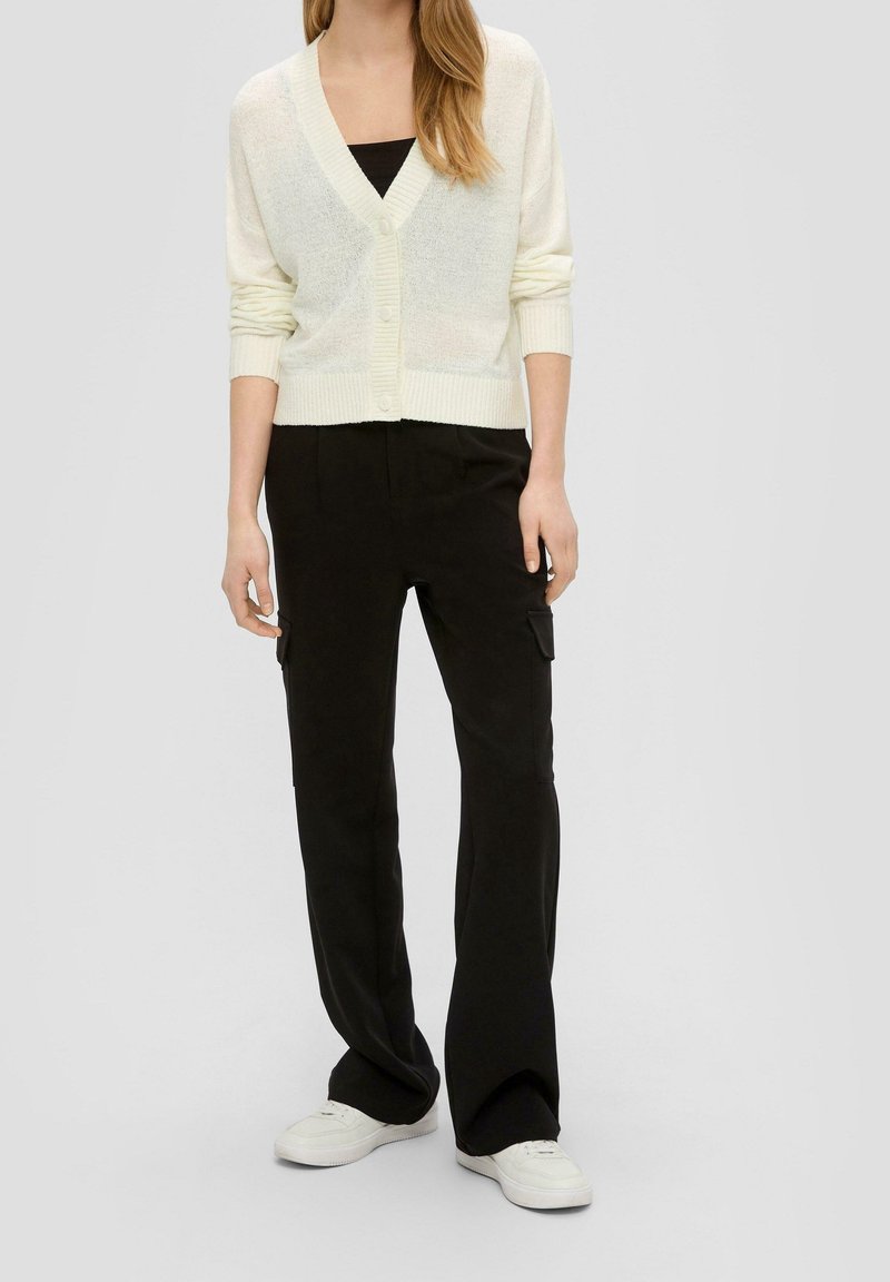 Ljusgrön öppen cardigan med v-ringning, mjuk textur och ribbade ärmslut, kombinerad med svarta cargobyxor och vita sneakers.