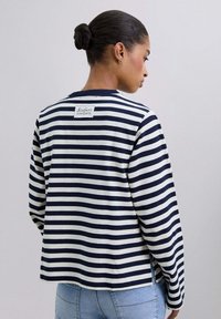 Camiseta de manga larga a rayas en azul marino y blanco, hecha de una tela suave, con un parche de logo en la parte posterior y aberturas laterales en el dobladillo.