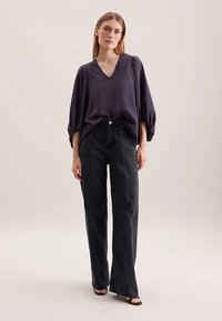 V-hals, mørkelilla bluse med løse ærmer, kombineret med højtaljede, sorte bukser med brede ben og sorte sandaler. Glat tekstur og enkelt design.