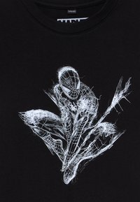 Melnā kokvilnas T-krekls ar baltu grafisku dizainu, kurā attēlota stilizēta, dinamiska zirnekļa figūra ar tīkla rakstu.